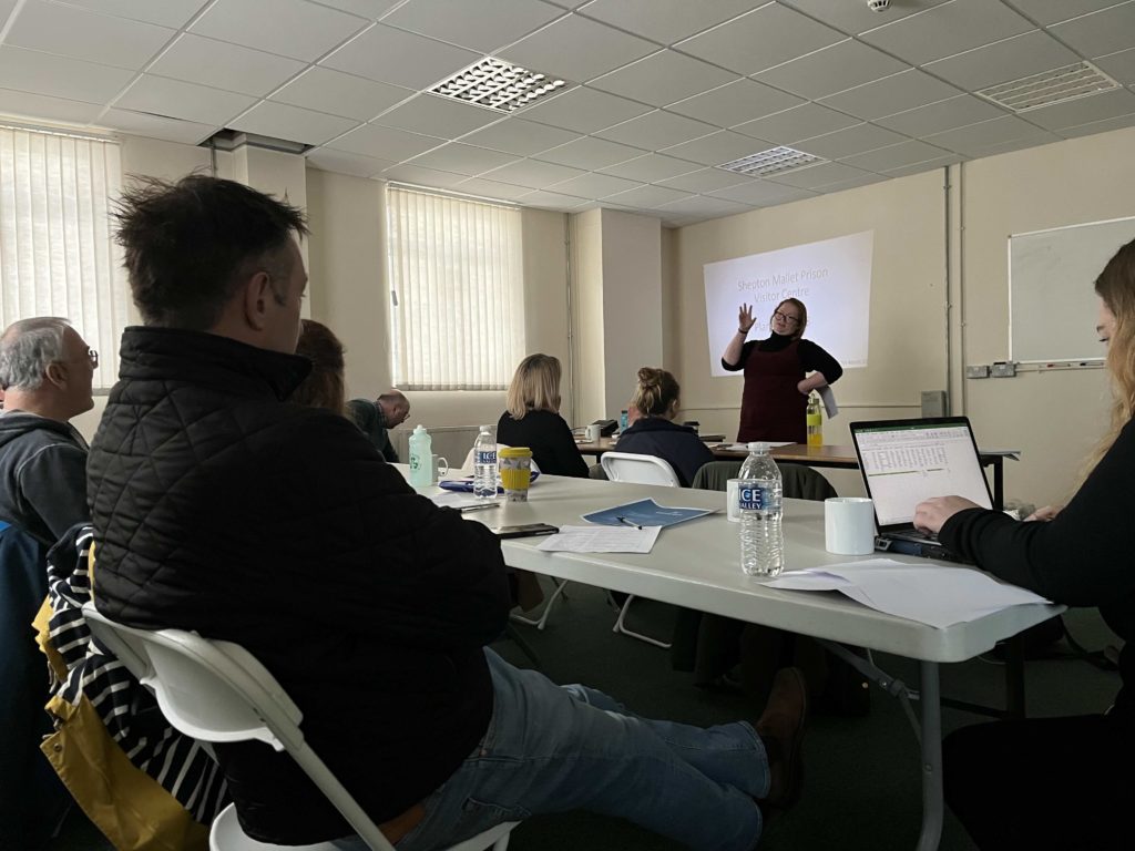 Group training session with a presenter speaking to seated attendees in a meeting room.